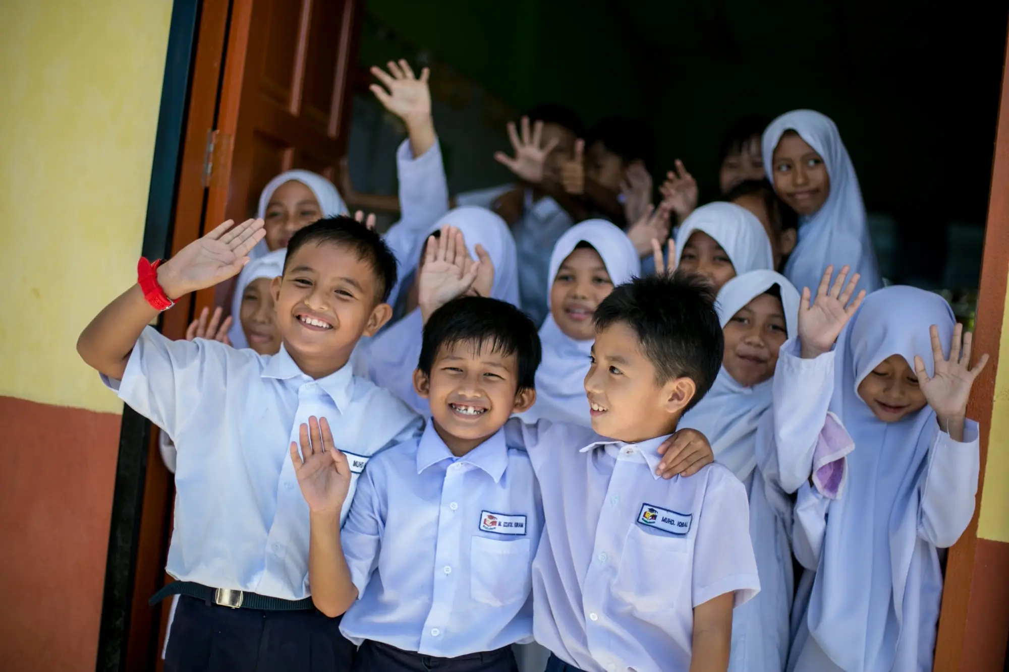 A crowd of primary pupils smiling and waving from a classroom doorway